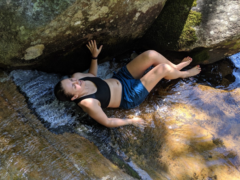 A woman in a sports bra grins while lounging in a mountain stream